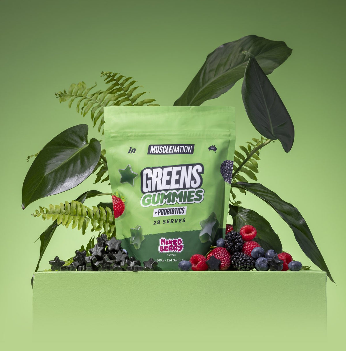 A pouch of Greens Gummies on a green plinth with leaves, berries and black star gummies