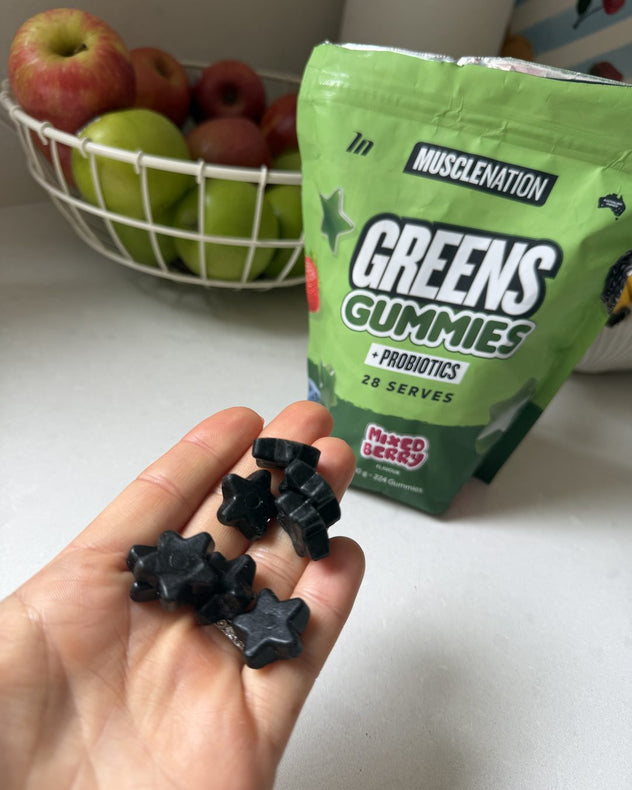 A handful of black star-shaped Greens Gummies in front of the pouch