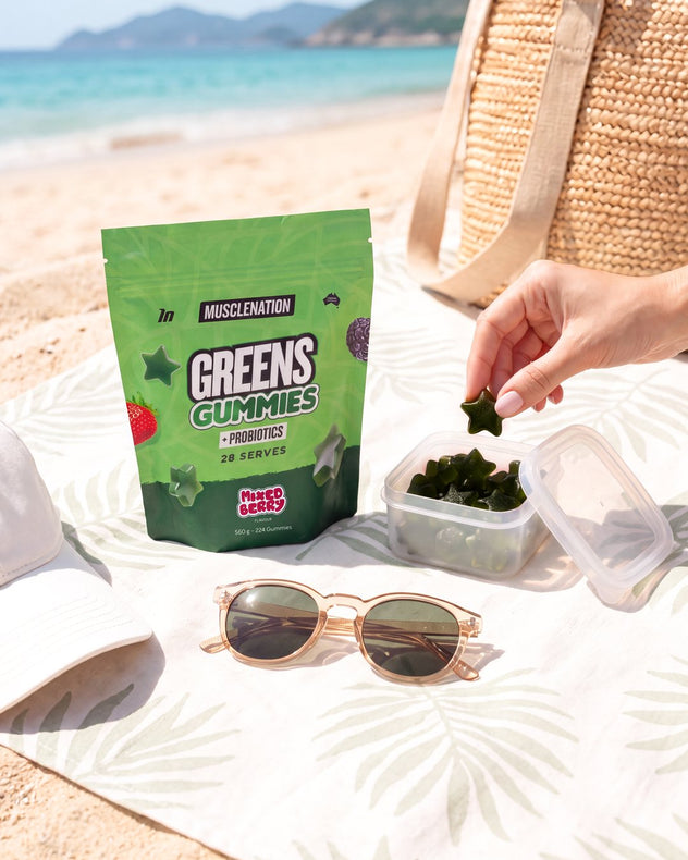 Taking a Greens Gummy from a tub on a beach towel beside the pouch